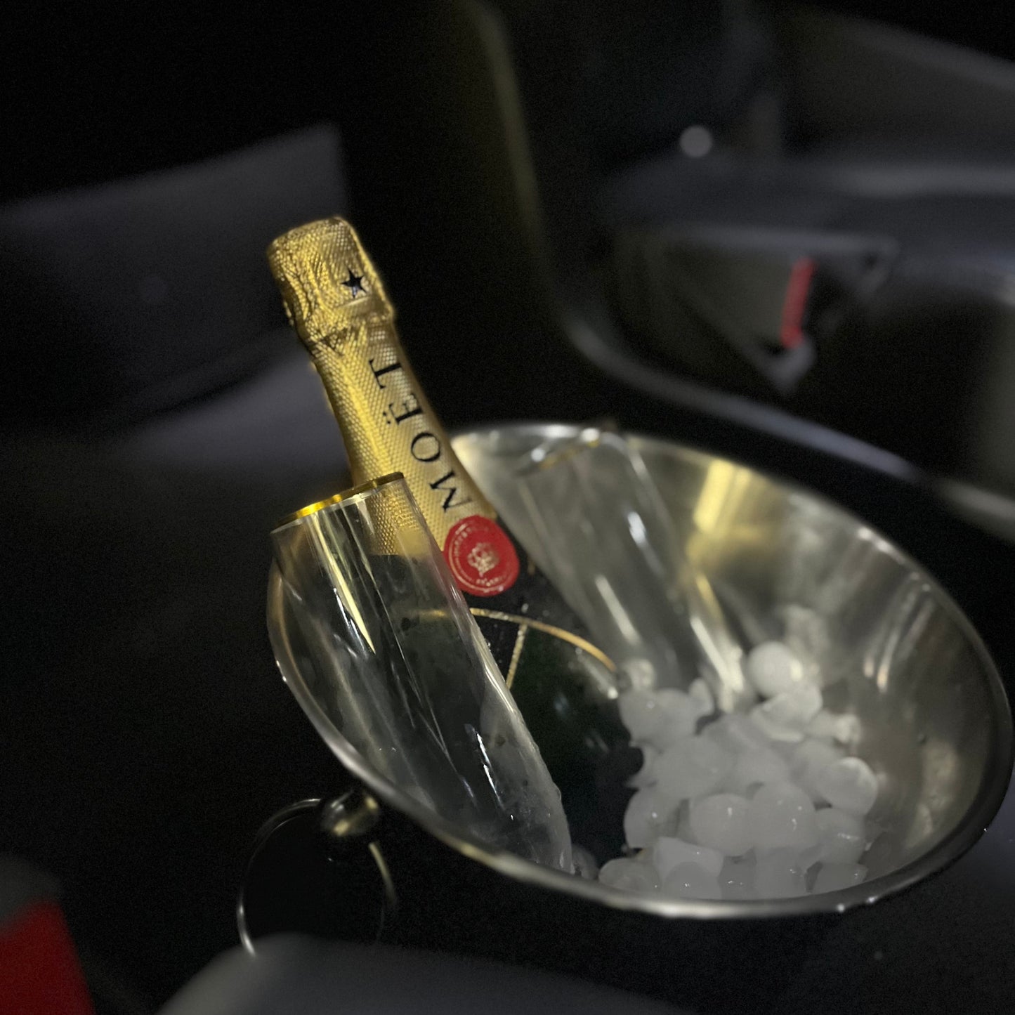 A bottle of Moët & Chandon champagne in a clear ice bucket, photographed inside a dark car interior.