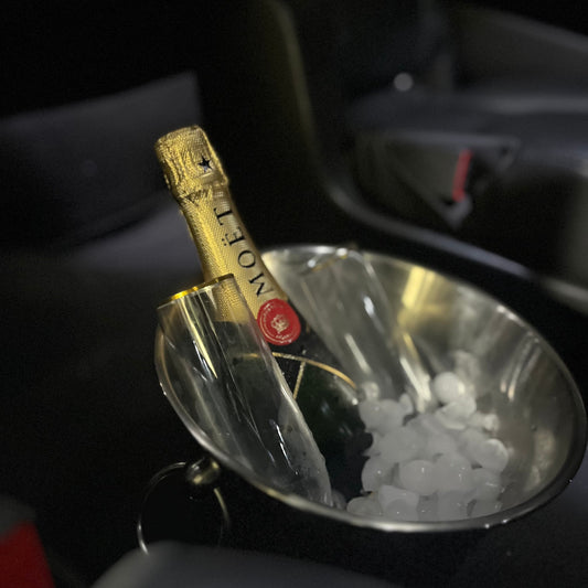 A bottle of Moët & Chandon champagne in a clear ice bucket, photographed inside a dark car interior.